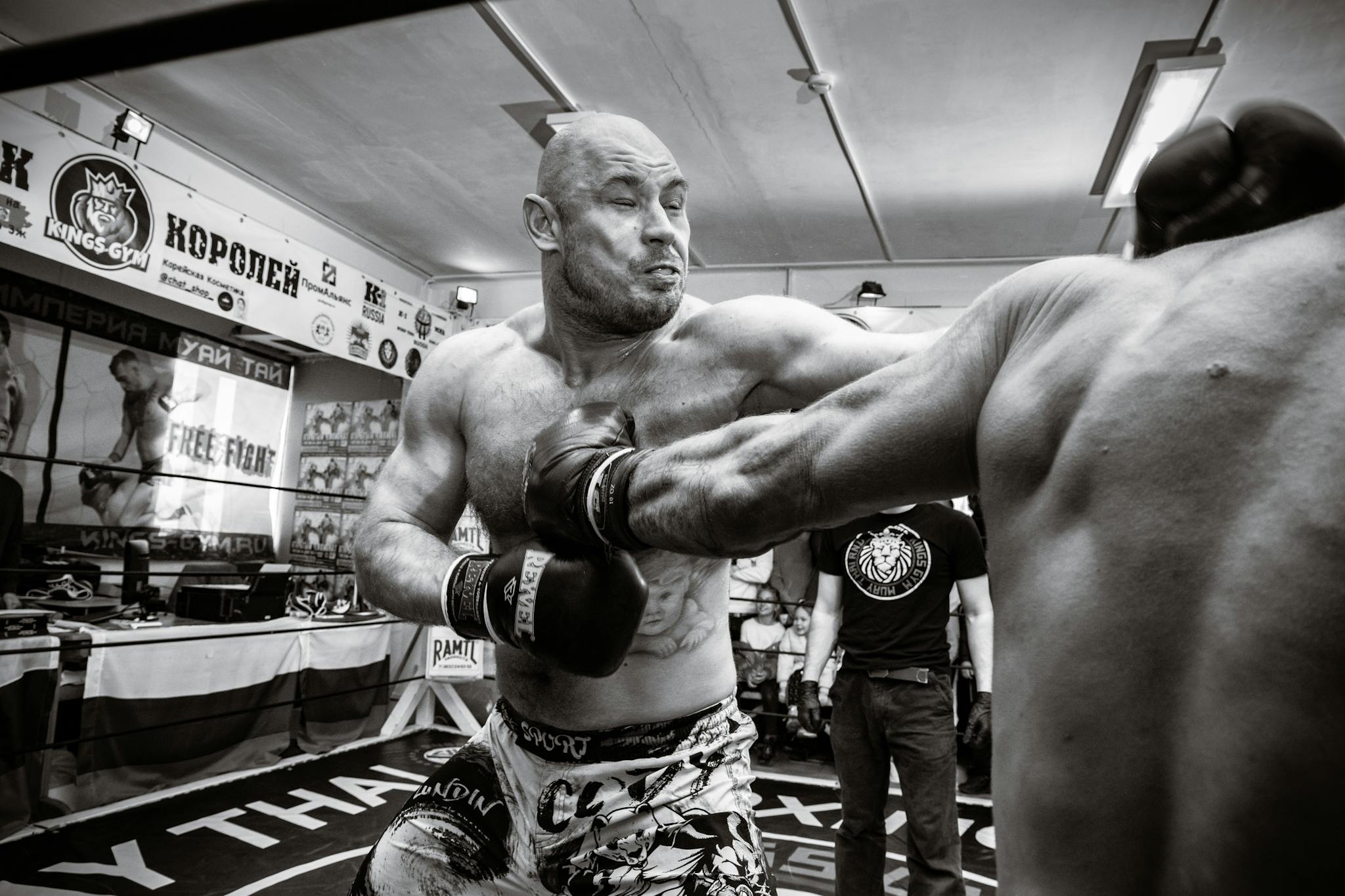 Grayscale image capturing intense action of MMA fighters in a gym setting with a punch in motion.