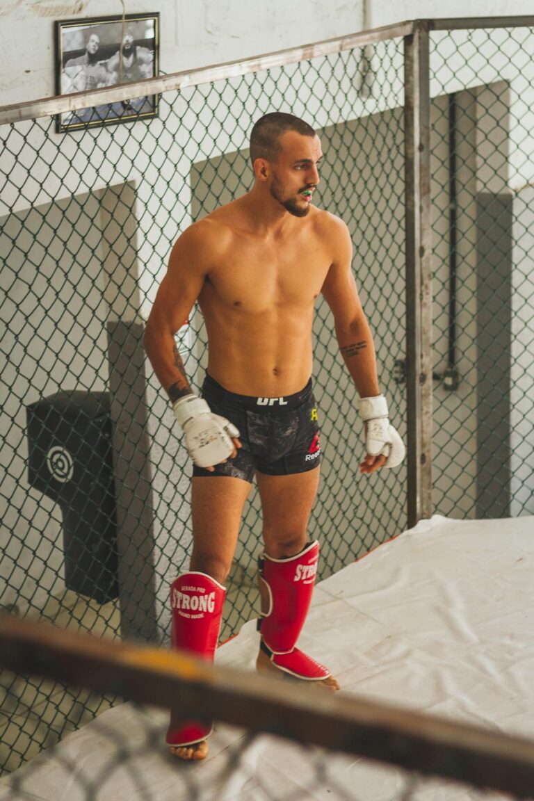 MMA fighter wearing shin guards and gloves preparing for practice in a training cage.