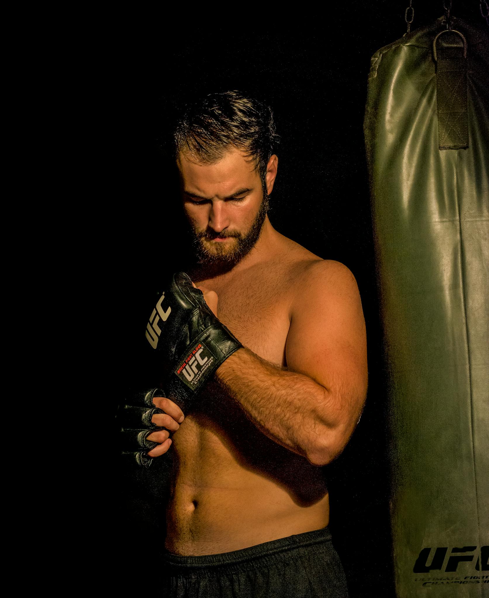 Strong male fighter with MMA gloves preparing for a training session with a punching bag, focused and determined.