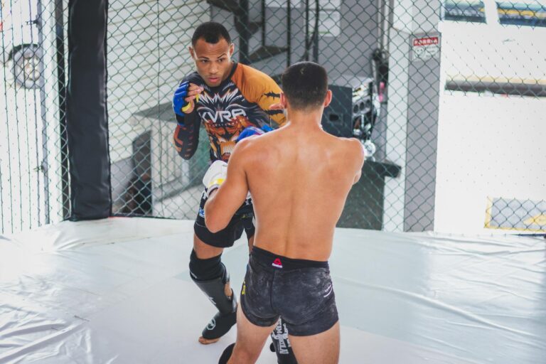 Two athletes engaged in a mixed martial arts sparring session inside a cage.
